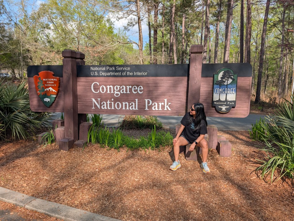 A woman sitting in front of the Congaree National Park sign